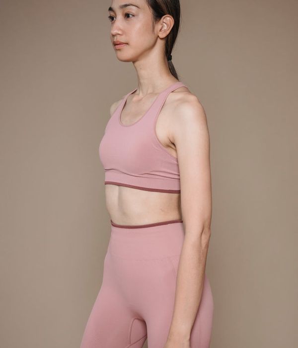 Woman in a graceful yoga pose against a powder pink background.